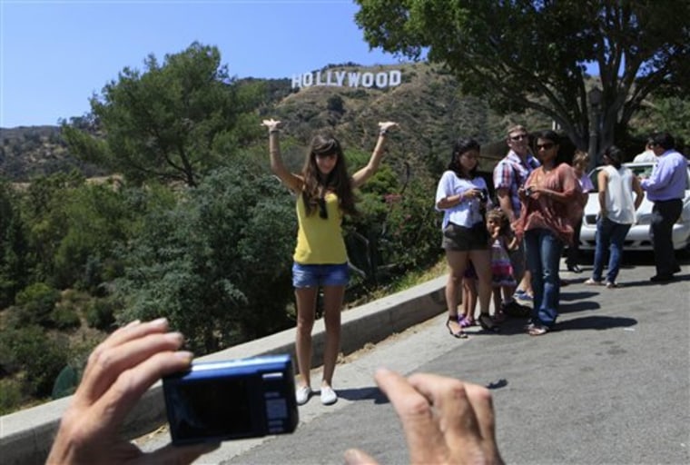 In this July 13, 2011 photo, tourists photograph each other on a hill with a view of the Hollywood sign in Los Angeles. The city’s iconic Hollywood sign may symbolize dreams of fame and fortune to many around the world, but to those who live in its shadow it means an endless stream of tourists and Times Square-style traffic jams. (AP Photo/Damian Dovarganes)